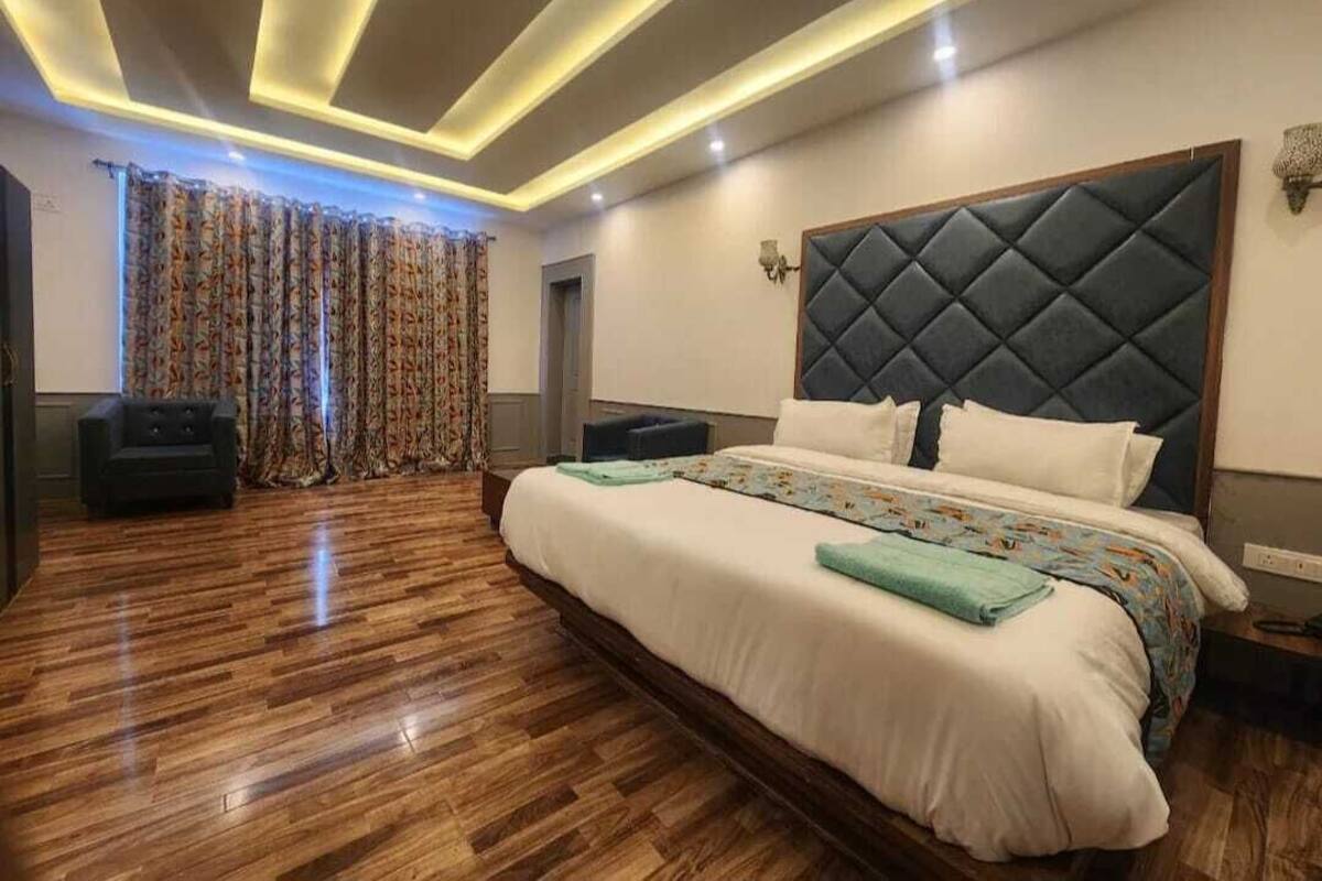 Quarto moderno com uma cama grande, piso de madeira e teto com iluminação embutida.