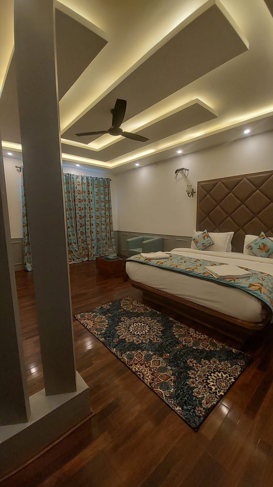 A modern bedroom with a large bed, a ceiling fan, and a patterned rug.