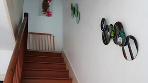 A wooden staircase with a handrail, white walls, and decorative wall art including a painting and circular mirrors.
