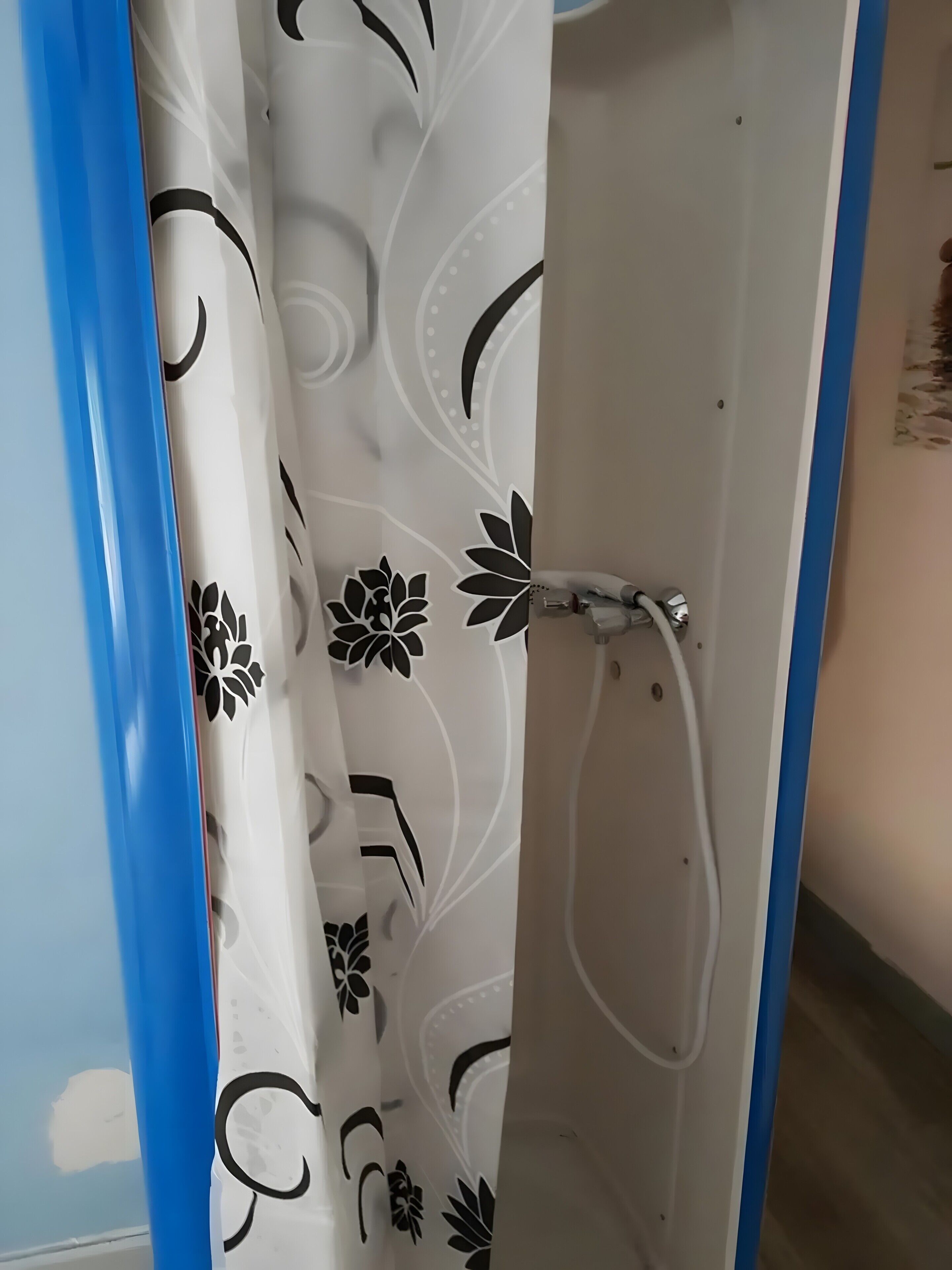 Une cabine de douche avec une porte blanche et un cadre bleu, un pommeau de douche et un rideau à motifs floraux.