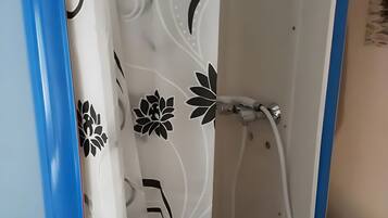 Une cabine de douche avec une porte blanche et un cadre bleu, un pommeau de douche et un rideau à motifs floraux.