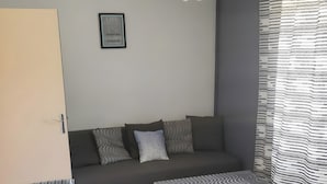 A modern living room with a sofa, a table, a bench, a hanging light fixture, and patterned curtains.