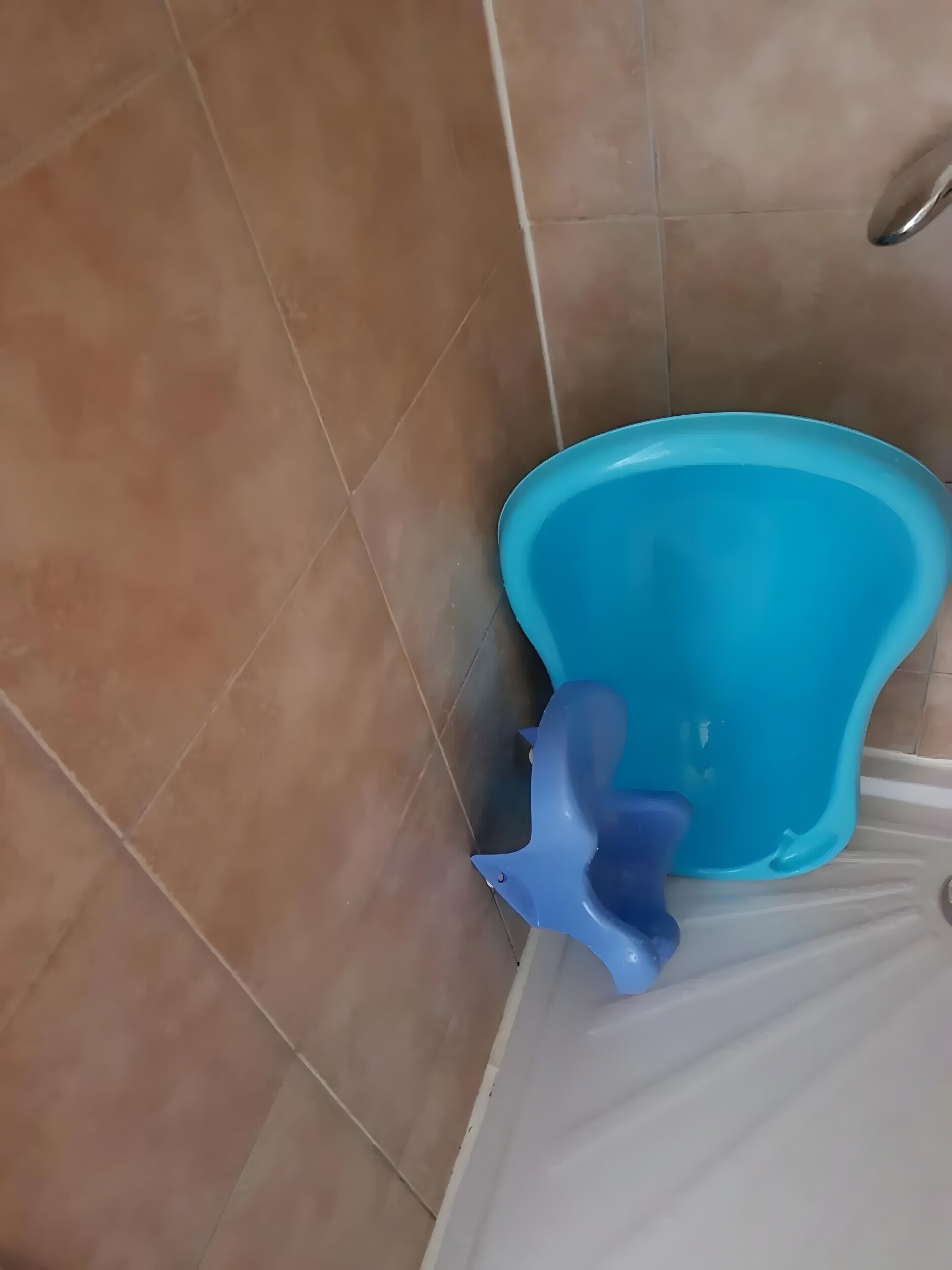 Un baño con inodoro azul, paredes de baldosas marrones y una zona de ducha blanca.