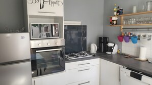 A modern kitchen with a built-in oven, microwave, and dishwasher. There are shelves with glassware and a coffee machine.