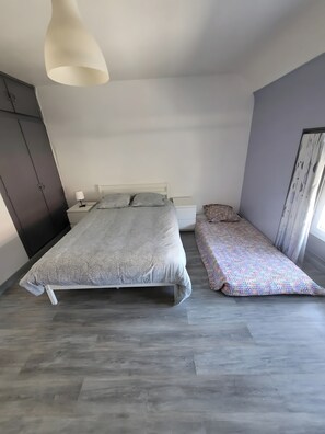 Ein Schlafzimmer mit Bett, Nachttisch, Lampe, Kleiderschrank und einem Fenster mit Vorhängen.
