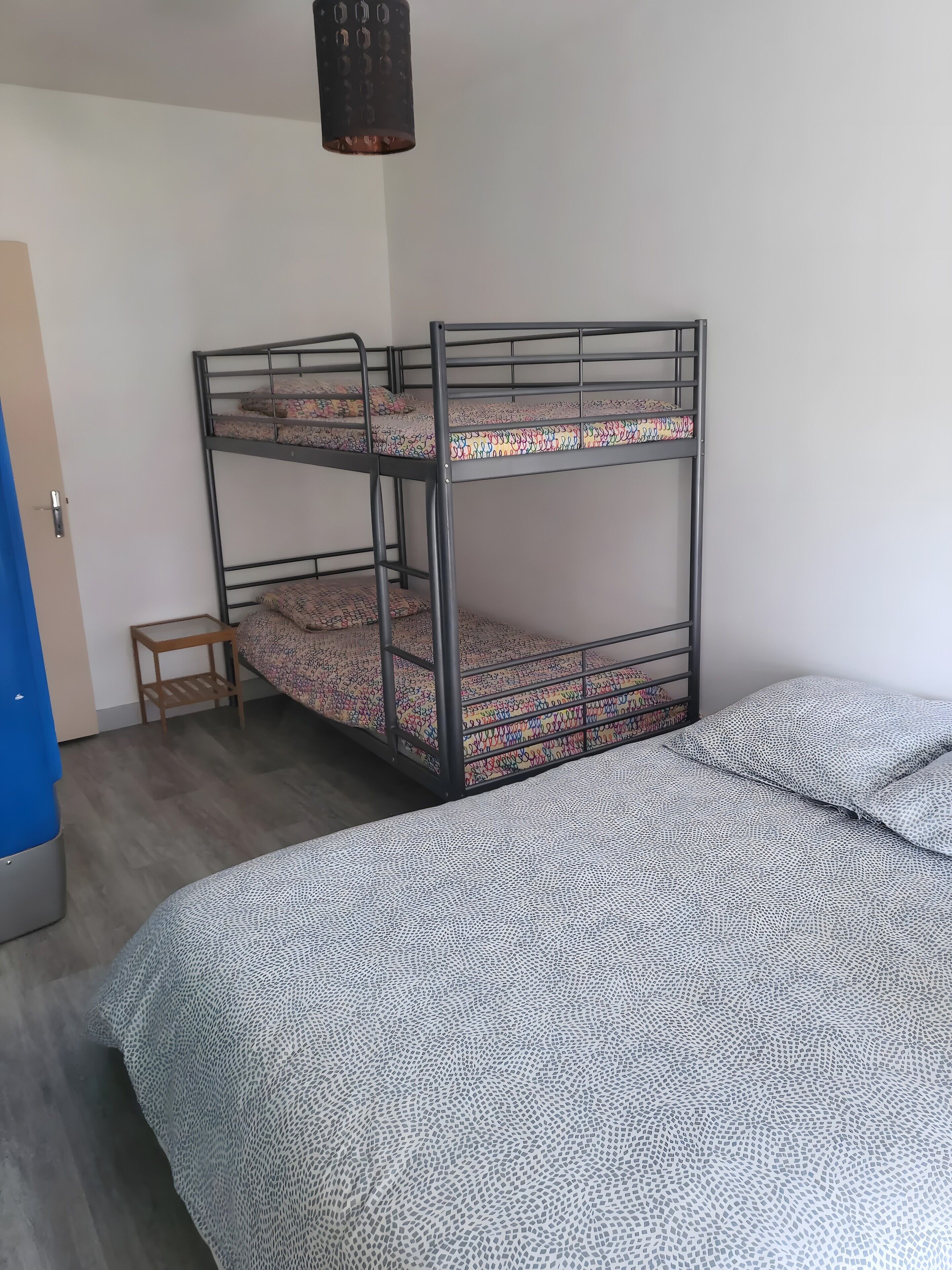Een stapelbed met beddengoed met een patroon, een klein houten krukje en een bed met een deken met geometrische patronen.