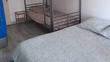 Een stapelbed met beddengoed met een patroon, een klein houten krukje en een bed met een deken met geometrische patronen.