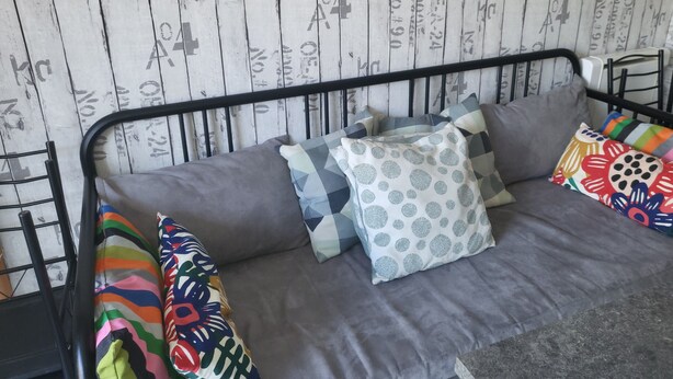 Un lit avec un cadre en métal, une literie grise et des coussins colorés.