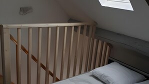 Une chambre avec un plafond en pente, une tête de lit en bois, un lit avec une literie blanche et un puits de lumière.