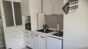 Une cuisine compacte avec des meubles blancs, un four à micro-ondes encastré, un évier et un petit réfrigérateur.