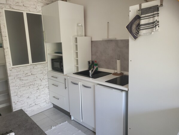 A compact kitchen with white cabinetry, a built-in microwave, a sink, and a small refrigerator.