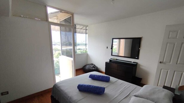 Quarto com cama, cômoda, espelho e porta de vidro deslizante que dá para uma varanda.