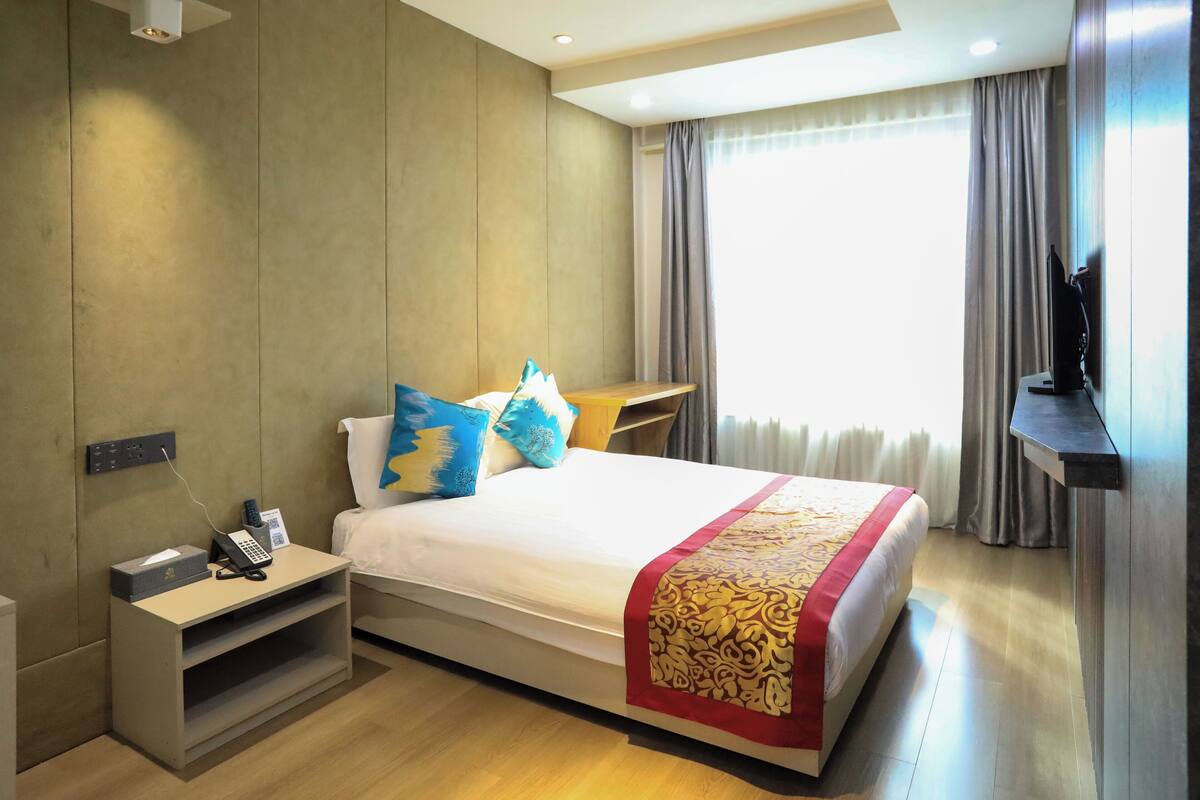 A hotel room with a bed, bedside table, and a desk with a chair.