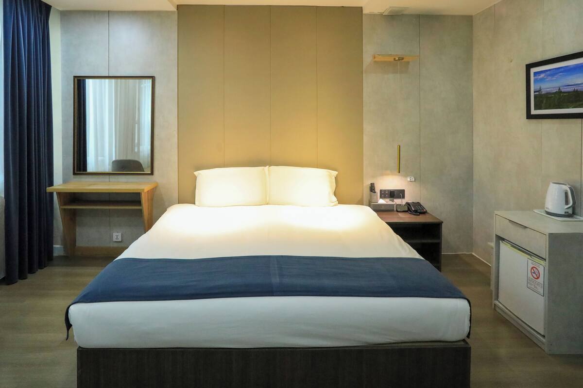 A hotel room with a bed, bedside table, desk, and a small cabinet.