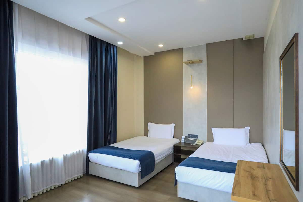 A hotel room with two beds, a wooden nightstand, a mirror, and a window with curtains.