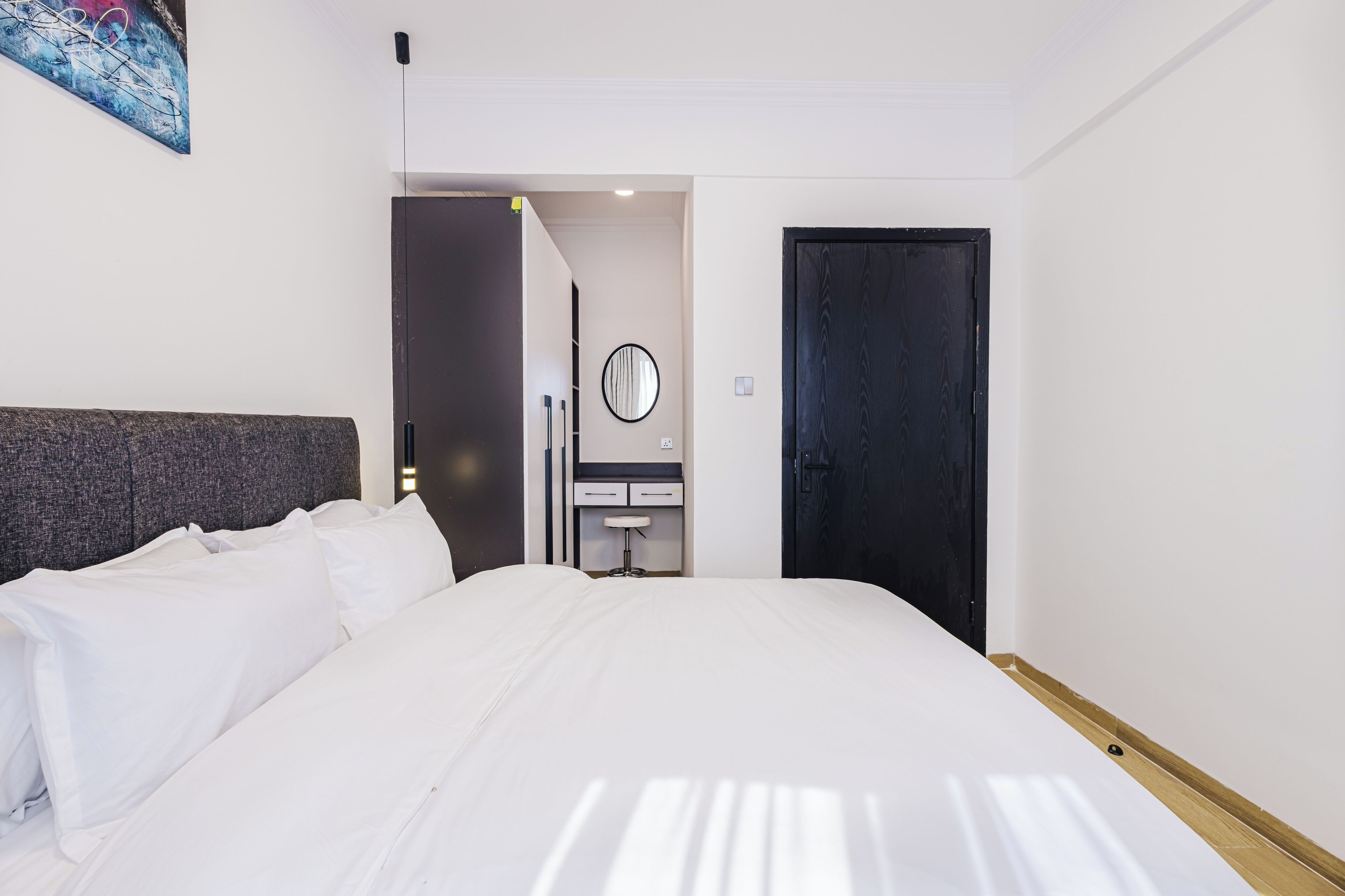 A hotel room with a large bed, a bedside table, a mirror, and a door.