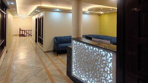 A hotel reception area with a marble floor, a reception desk with a decorative back panel, a blue sofa, and a staircase leading to another floor. - Hotel The Waypoint Inn (Shimla)