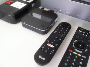 Un televisor, un control remoto negro y un dispositivo negro con pantalla sobre una superficie blanca.
