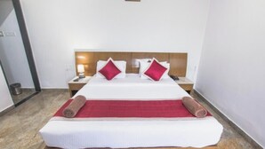 A hotel room with a wooden bed, white bedding, two red pillows, a red throw blanket, and a wooden headboard. - Hotel Sarayu Hassan (Hassan)