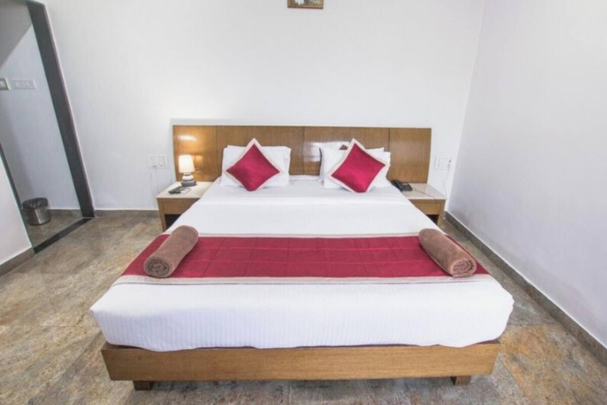 Quarto de hotel com cama de madeira, roupa de cama branca, duas almofadas vermelhas e manta vermelha, além de cabeceira de madeira.