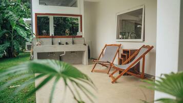 A modern outdoor kitchen area with a concrete countertop, two wooden chairs, and a large window overlooking greenery.