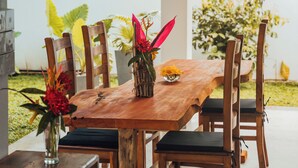 A wooden dining table with chairs, a vase with flowers, and a small bowl of yellow flowers.