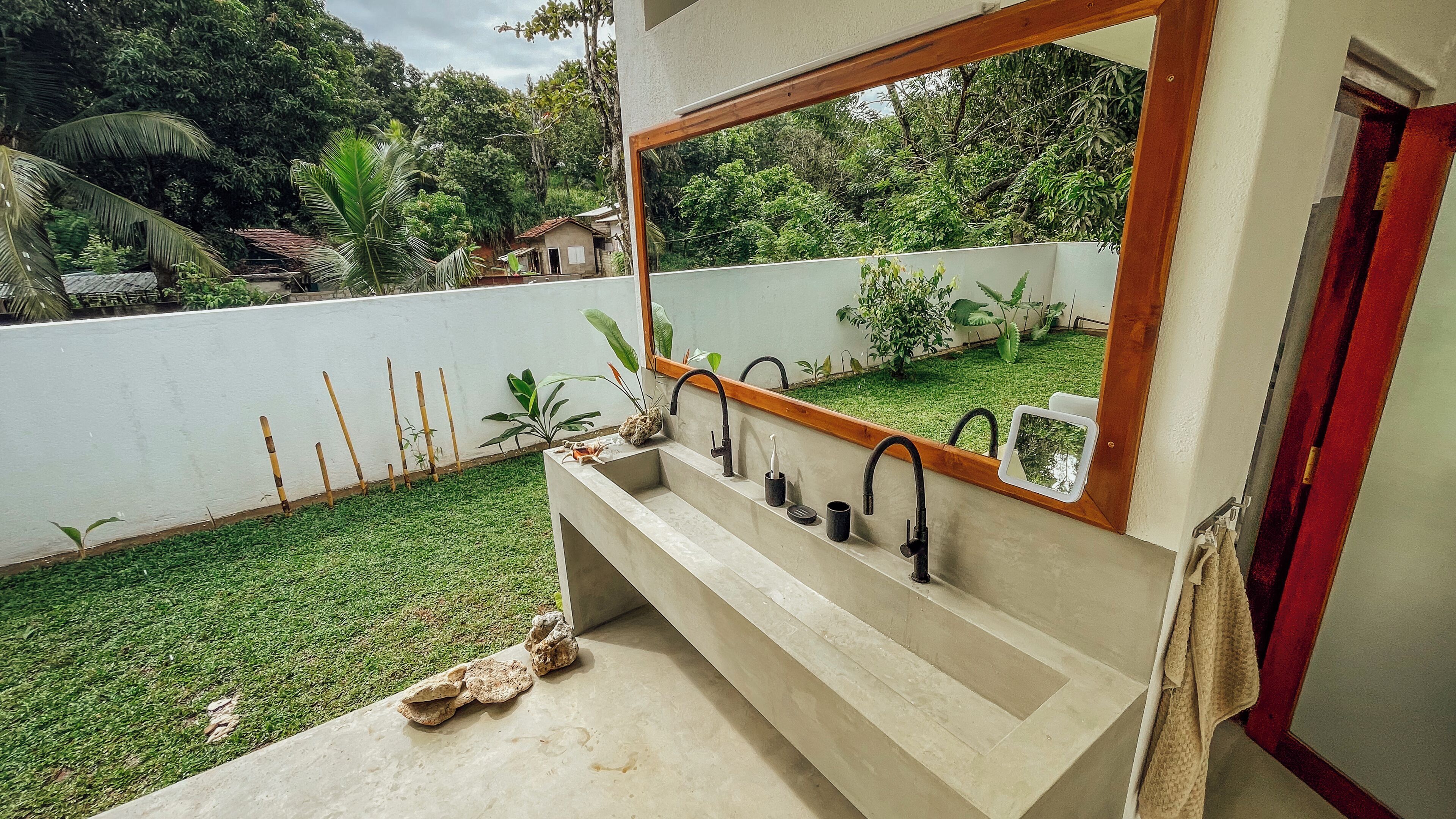 A bathroom with a large mirror, multiple sinks, and a small garden area visible through the window.