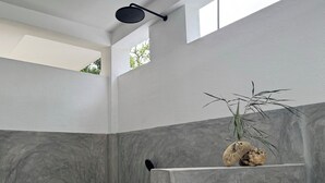 A modern bathroom with a shower, a stone wall, and a plant.