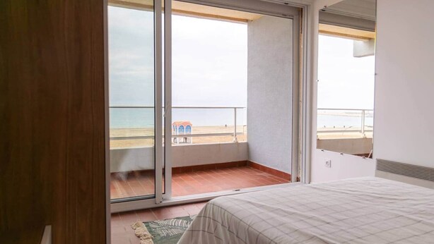 Un dormitori amb una gran porta corredissa de vidre que dona a un balcó amb vista a la platja.