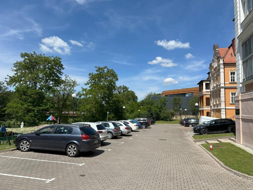 Een parkeerplaats met meerdere auto's die in rijen geparkeerd staan, naast een gebouw met klassieke architectuur.