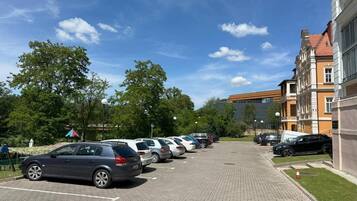 Een parkeerplaats met meerdere auto's die in rijen geparkeerd staan, naast een gebouw met klassieke architectuur.