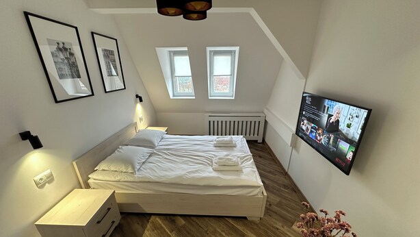 Moderni makuuhuone, jossa on sänky, yöpöydät, televisio ja patteri.