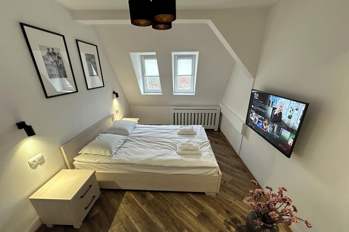 A modern bedroom with a bed, bedside tables, a TV, and a radiator.