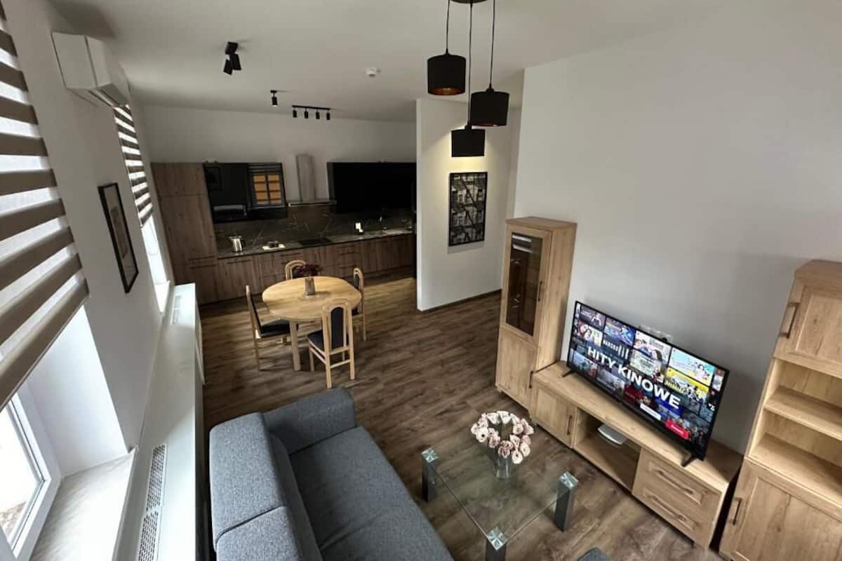 A modern living room with a grey sofa, a coffee table with flowers, a TV, and a wooden cabinet.