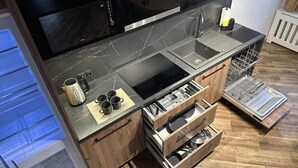 A compact kitchen with a black countertop, a built-in oven, and wooden cabinetry. - Nysa River Apartments (Zgorzelec)