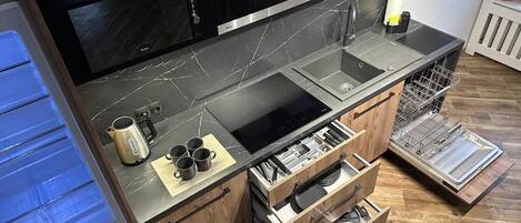 A compact kitchen with a black countertop, a built-in oven, and wooden cabinetry.