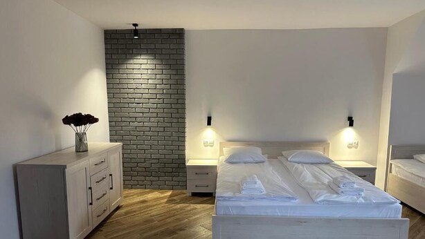 A bedroom with a wooden floor, a white bed, a nightstand, a dresser, and a brick accent wall. - Nysa River Apartments (Zgorzelec)