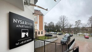 A NYSARIVER APARTMENTS sign with a contact number, a staircase, and a parking lot with cars. - Nysa River Apartments (Zgorzelec)