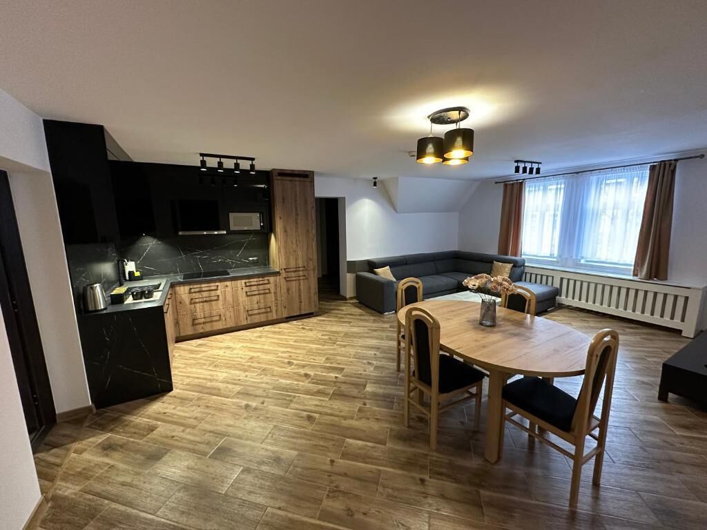 A modern kitchen with a black countertop, wooden cabinets, and a dining area with a wooden table and chairs.