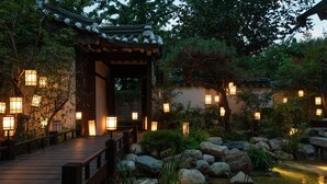 Perinteinen japanilainen puutarha, jossa on puinen silta, lyhdyt, kivet ja lampi.