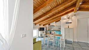 A spacious living area with a high wooden ceiling, a dining table with chairs, a green sofa, and a kitchen area with a tiled backsplash. - 2 bedroom stunning apartment in Agropoli (Agropoli)