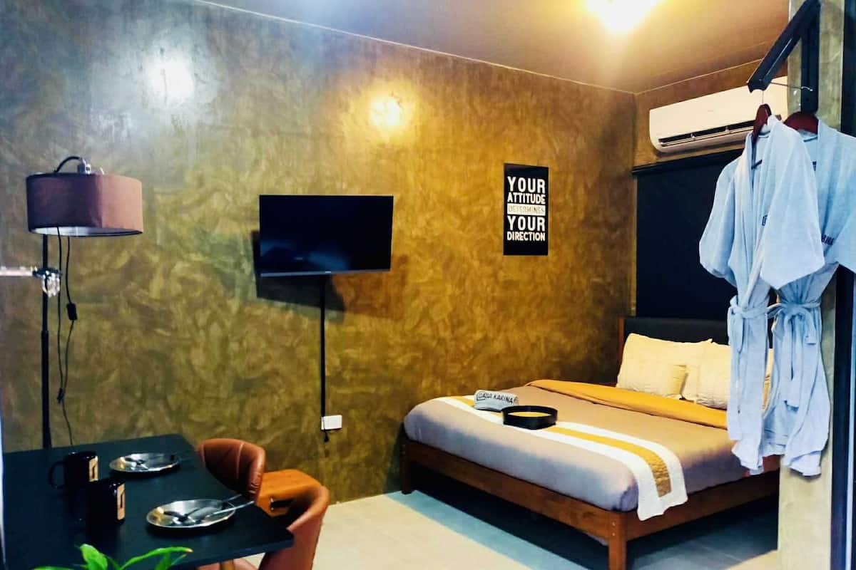 A hotel room with a bed, a TV, a desk with a chair, and a robe hanging on the wall.