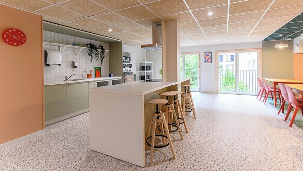 A modern kitchen with a central island, bar stools, and a red clock on the wall. - Student Factory Paris - Universeine  (Saint-Denis)