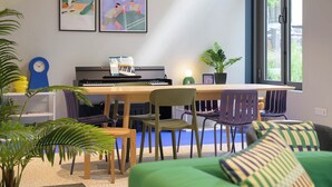 A room with a piano, chairs, a table, and two framed artworks on the wall. - Student Factory Paris - Universeine  (Saint-Denis)