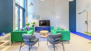 A modern living room with green sofas, two armchairs, a coffee table, and a TV on a stand. - Student Factory Paris - Universeine  (Saint-Denis)