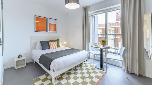 Een moderne hotelkamer met een bed, nachtkastje en een tafeltje met een plant.