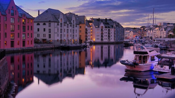 Un hotel frente al río con varios pisos, un muelle con barcos y un río tranquilo que refleja los edificios.