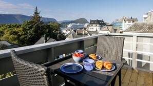Un balcón con una mesa dispuesta para el desayuno, con vistas a un paisaje montañoso y un crucero.