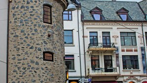 Una calle empedrada con edificios históricos, incluyendo una torre de piedra y un edificio con balcón.