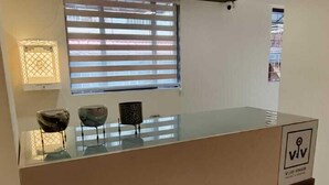 Un mostrador de recepción con un reloj, una ventana con persianas y un ventilador de techo.